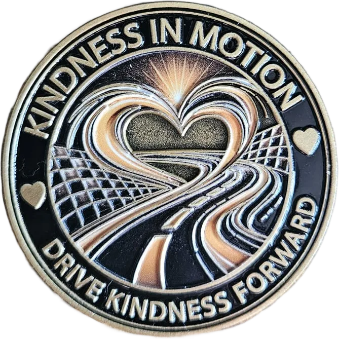 Front of the Kindness in Motion coin: a heart formed from a winding road with checkered-flag edges, ringed by the words Kindness in Motion — Drive Kindness Forward